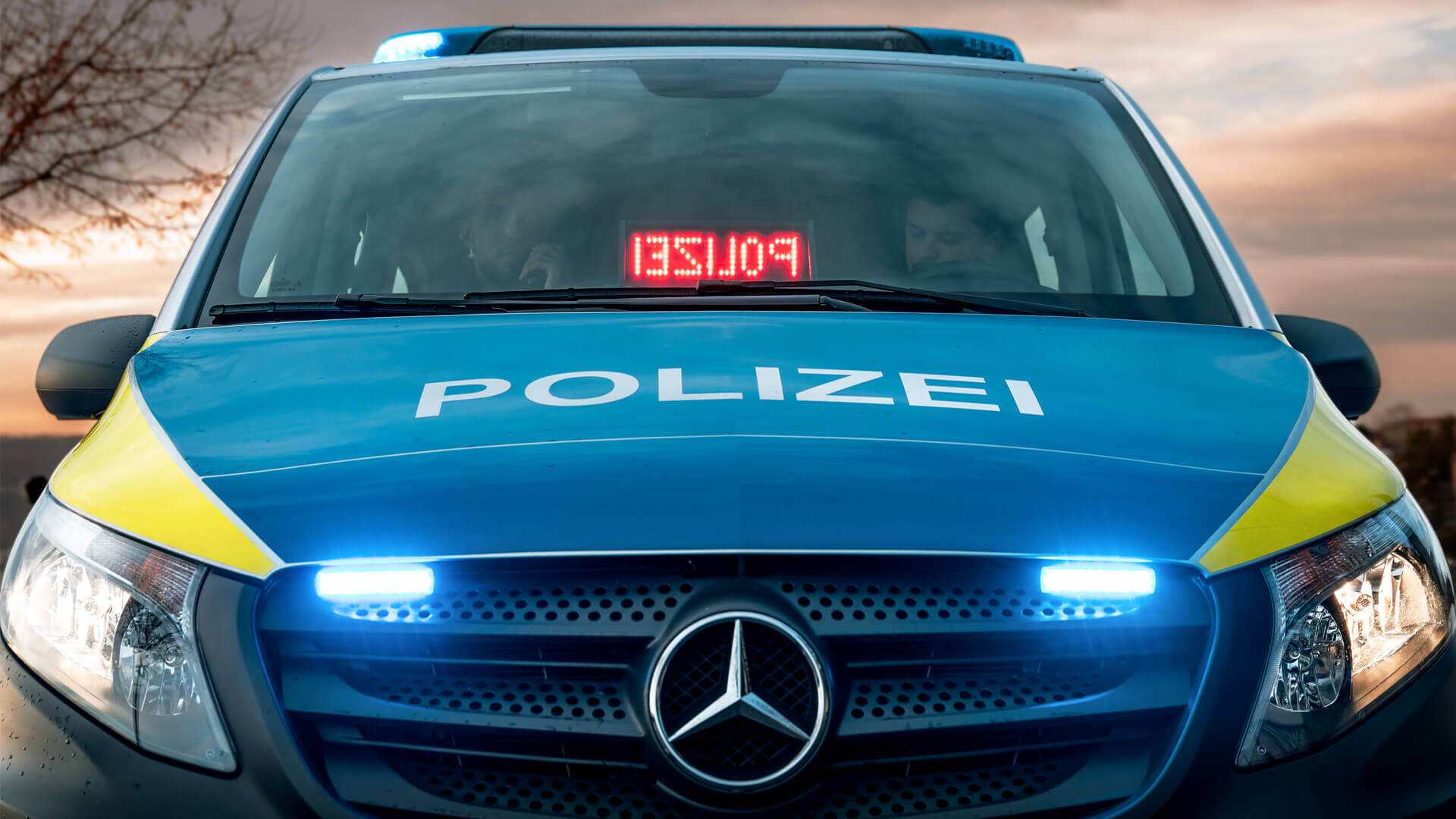 Ein Polizeiauto mit eingeschaltetem Blaulicht ist zu sehen. Das Auto wird von zwei Polizisten besetzt, die im Auto sitzen. Die Polizeileuchte auf dem Dach des Autos blinkt und signalisiert, dass ein Fahrzeug gebeten wird, anzuhalten. Das Bild suggeriert eine polizeiliche Aktivität oder einen Einsatz.