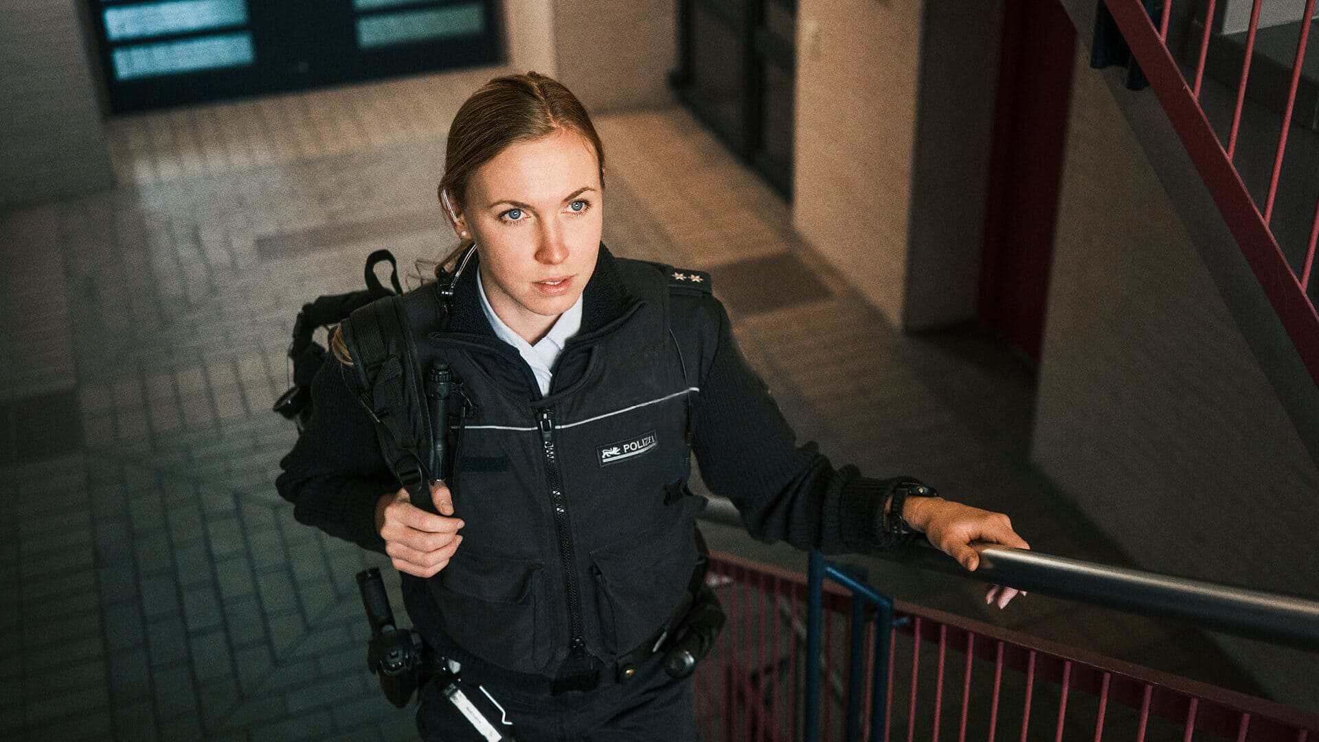 Bild von Polizistin Vivien in Uniform, die einen Rucksack über der Schulter trägt und eine Treppe hochgeht.